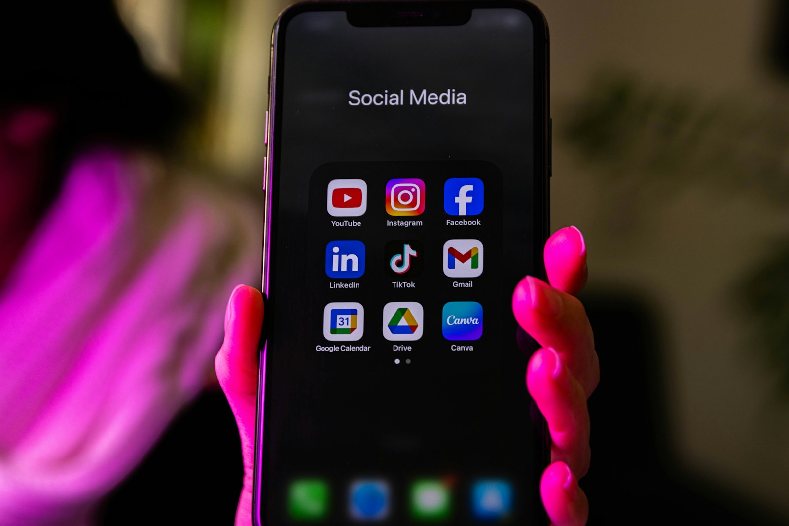 A hand holding a phone showing a folder of social media apps