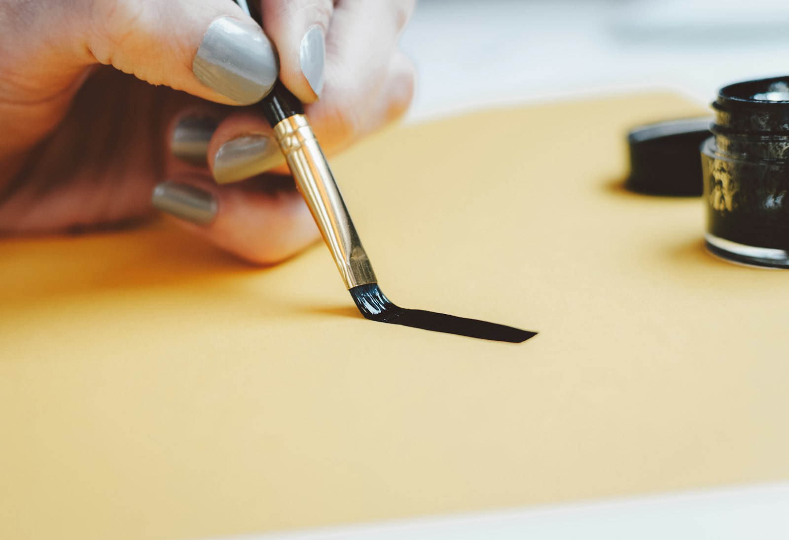 A hand drawing a single black brush stroke on cream paper
