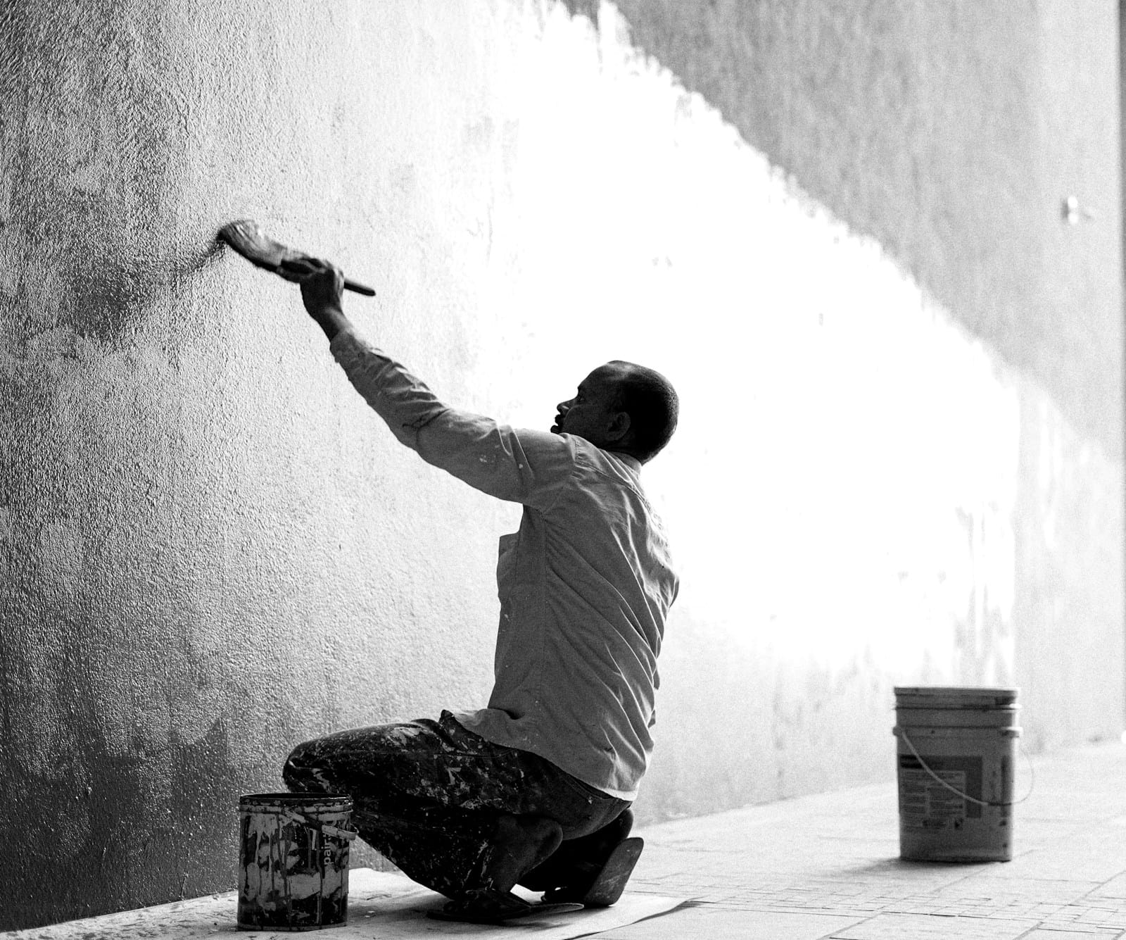 A man repainting a bare wall, in black and white