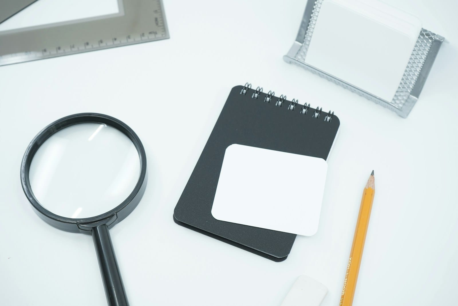 A magnifying glass and a blank notepad on a white desk